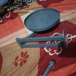 May include: A grey metal swivel stand featuring a circular top plate attached to a horizontal support arm. The base of the arm has a circular mounting plate partially covered in clear plastic film. The structure is finished in a smooth grey paint.