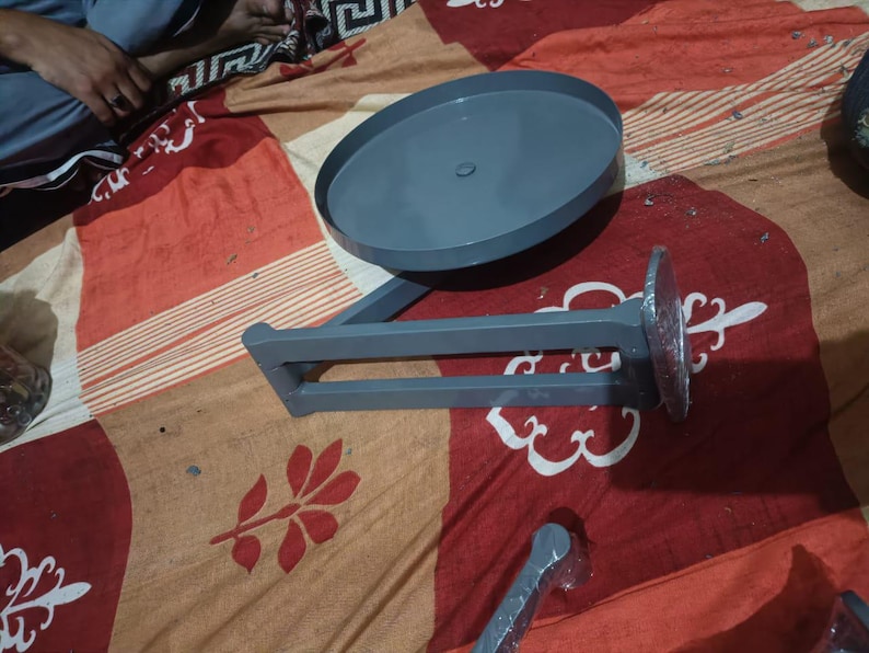 May include: A grey metal swivel stand featuring a circular top plate attached to a horizontal support arm. The base of the arm has a circular mounting plate partially covered in clear plastic film. The structure is finished in a smooth grey paint.