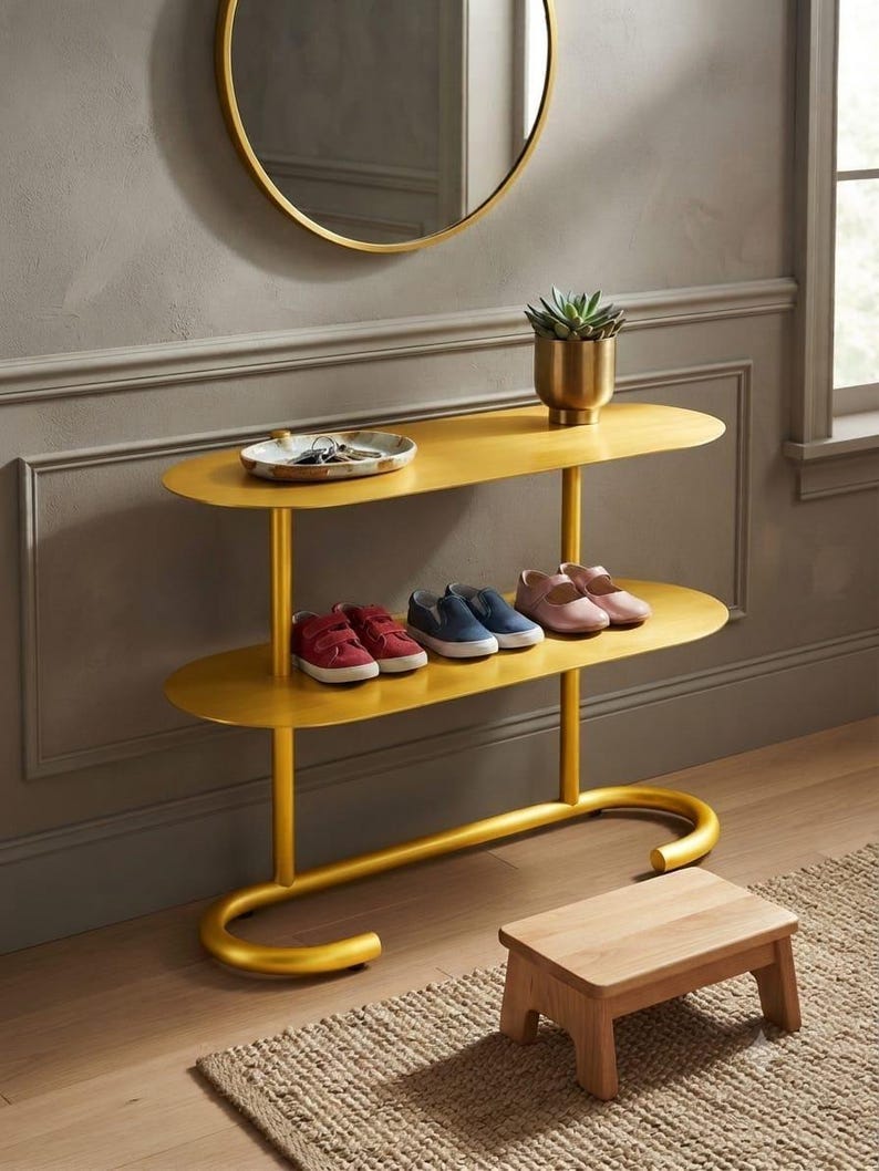 May include: A two-tier gold metal console table with oval shelves, featuring a small succulent in a gold pot and a shallow dish with keys on the top shelf, and three pairs of children's shoes on the bottom shelf, positioned near a wooden stool.