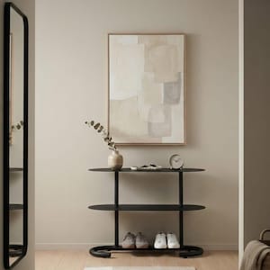 May include: A black metal console table with two oval shelves, featuring a light-coloured abstract painting in a wooden frame above it. On the top shelf sits a small vase with eucalyptus stems, a decorative tray, and a round analogue clock.