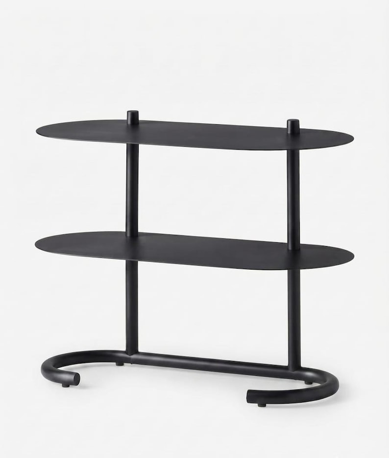 May include: A matte black metal shelving unit featuring two oval-shaped shelves supported by two vertical cylindrical posts. The base consists of a curved, U-shaped tubular frame that provides stability, creating a clean and functional storage structure.