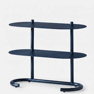 May include: A dark navy blue metal shelving unit featuring two oval-shaped shelves supported by two vertical cylindrical posts. The base consists of a curved, U-shaped tubular frame that provides stability, with a smooth, matte finish throughout.