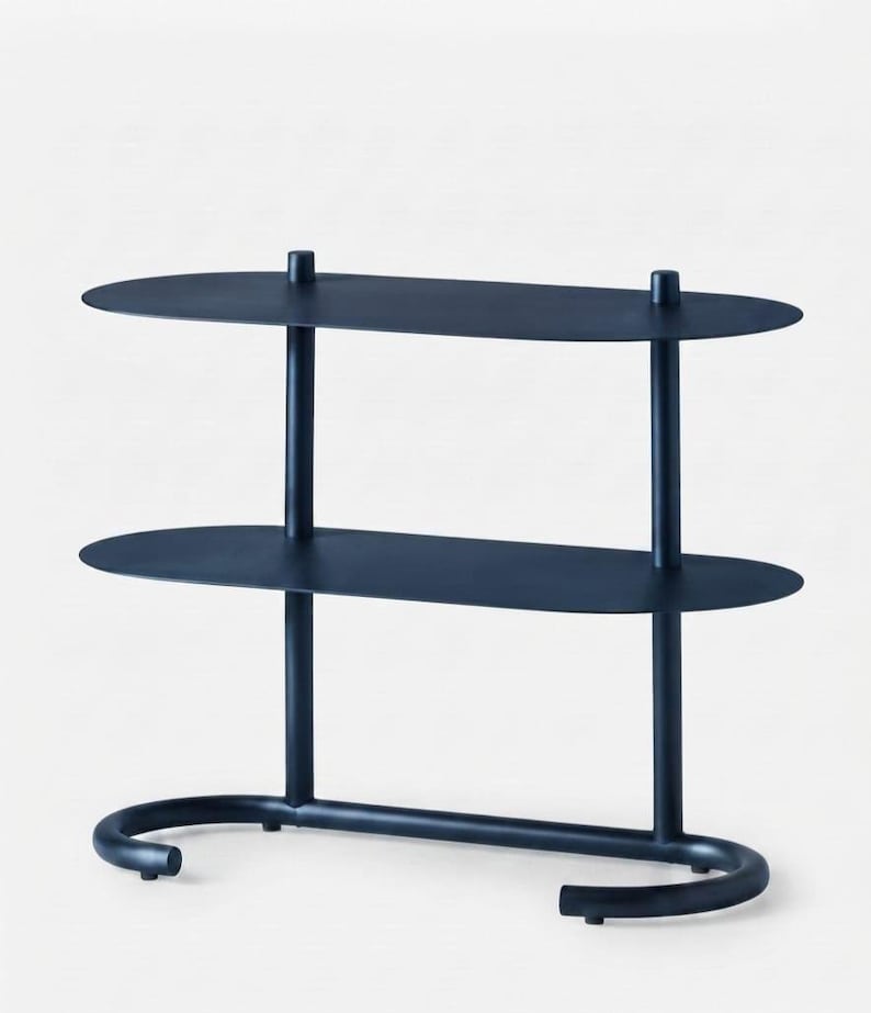 May include: A dark navy blue metal shelving unit featuring two oval-shaped shelves supported by two vertical cylindrical posts. The base consists of a curved, U-shaped tubular frame that provides stability, with a smooth, matte finish throughout.