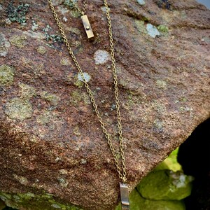 Könnte beinhalten: Zwei goldene Halsketten mit rechteckigen Anhängern. Der obere Anhänger ist schlicht und der untere Anhänger trägt die Gravur "FE515 1935".