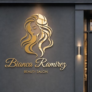 Op de afbeelding: Een donkergrijze buitenmuur met een goudkleurig logo van een vrouwenprofiel met golvend haar boven de tekst Bianca Ramirez BEAUTY SALON in een gouden scriptlettertype, naast een glazen deur met een zwart frame en een kleine plant.