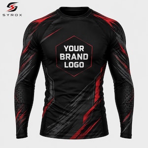 Pode incluir: Camiseta esportiva preta de manga comprida com elementos de design abstratos vermelhos e cinzentos. A camisa apresenta gola redonda e uma área de logotipo em forma de hexágono com o texto "YOUR BRAND LOGO" em branco. O logotipo Syrox está no canto superior esquerdo.