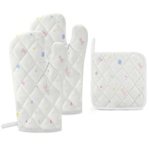 May include: A set of three white quilted kitchen items: two oven mitts and a pot holder. The items are decorated with a repeating pattern of pink bows, blue flowers, and yellow dots. The mitts have a loop for hanging.