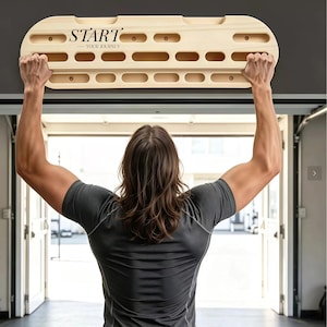 Può includere: Una tavola da allenamento in legno chiaro per l'arrampicata, dotata di molteplici fessure e tasche orizzontali di varie dimensioni. Il testo "START YOUR JOURNEY" è stampato in nero sul lato sinistro della tavola, montata orizzontalmente.