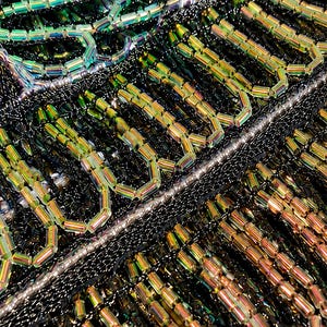 May include: A textile surface featuring intricate embroidery with black seed beads and iridescent green, gold, and silver bugle beads arranged in geometric patterns. The design includes rows of cylindrical beads creating a textured, reflective finish.