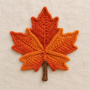 Peut inclure: Une feuille d'érable crochetée présentant un dégradé de fils orange, rouge et jaune vifs. La feuille possède cinq lobes pointus distincts avec des nervures texturées en relief partant du centre et une courte tige marron à la base.
