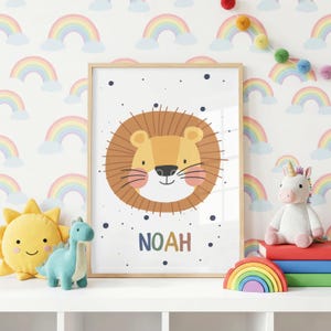 Puede incluir: Una lámina enmarcada con la cara de un león de dibujos animados con melena marrón y el nombre NOAH impreso en letras multicolores debajo. El diseño está decorado con puntos azul oscuro sobre fondo blanco, junto a peluches y libros.