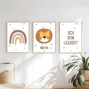 Puede incluir: Tres láminas decorativas enmarcadas que muestran un arcoíris marrón, una cara de león de dibujos animados con el nombre NOAH y el texto ICH BIN GELIEBT en letras de colores. Cada impresión blanca tiene puntos azul oscuro y un marco de madera clara.