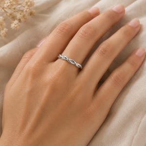 Op de afbeelding: Een gepolijste zilverkleurige ring met een delicaat gedraaid touwontwerp. De band bestaat uit twee dunne metalen strengen die in elkaar zijn gevlochten om een doorlopend, uniform spiraalpatroon te creëren dat de vinger omsluit met een gladde afwerking.