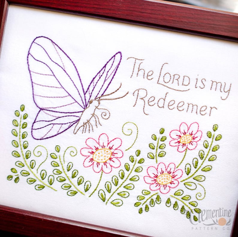 May include: Embroidered artwork in a dark wood frame. The design features a purple butterfly, pink flowers, and green foliage. Text reads "The LORD is my Redeemer". A decorative piece for home decor.