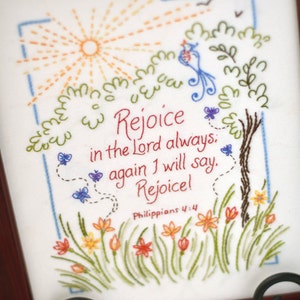 May include: Embroidered artwork with a sun, birds, butterflies, flowers, and a tree. The text reads "Rejoice in the Lord always, again I will say. Rejoice!" Philippians 4:4