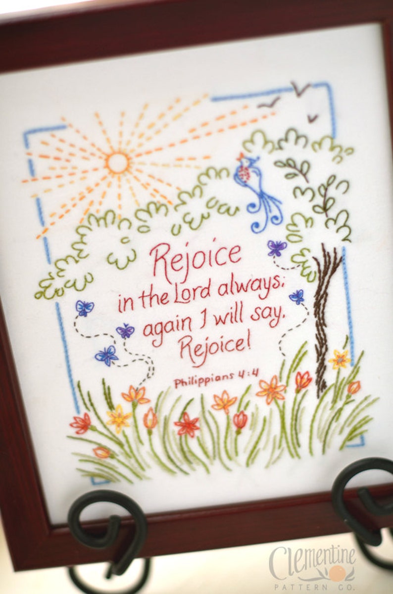 May include: Embroidered artwork with a sun, birds, butterflies, flowers, and a tree. The text reads "Rejoice in the Lord always, again I will say. Rejoice!" Philippians 4:4