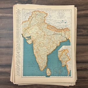 May include: A stack of vintage maps featuring a detailed map of India, with a teal blue ocean and tan landmass. The map is from the "World Atlas and Gazetteer". The map is printed on aged paper.
