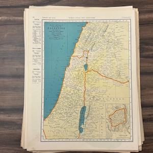 Puede incluir: Una pila de mapas antiguos, con el mapa superior que presenta una ilustración detallada de Palestina. El mapa tiene un mar azul, tierra beige y bordes naranjas. El texto incluye "Palestina" y otros detalles geográficos.