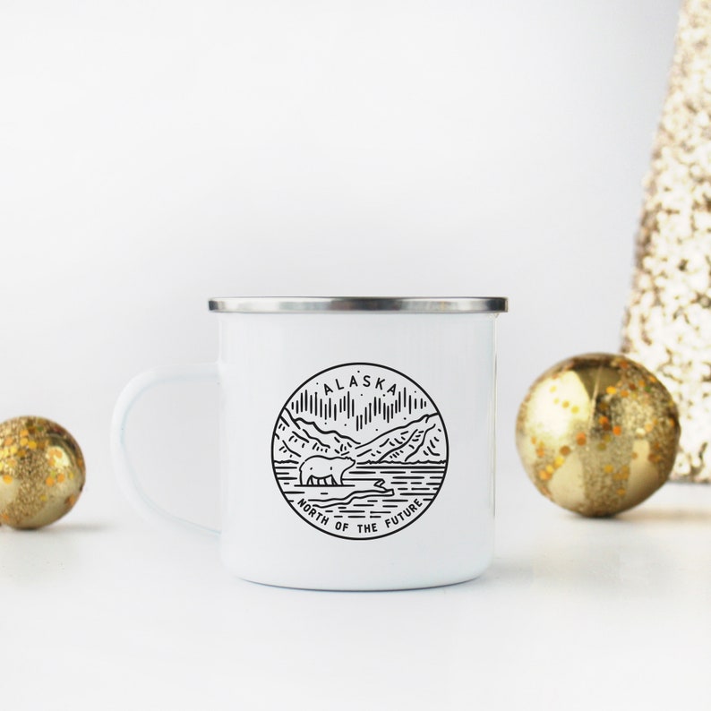 Puede incluir: Taza de camping de esmalte blanco con un gr&aacute;fico en blanco y negro de un oso y monta&ntilde;as. El gr&aacute;fico est&aacute; en un c&iacute;rculo con el texto "Alaska North of the Future".