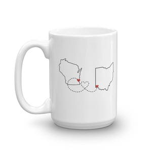 May include: White ceramic coffee mug with a black outline of the states of Wisconsin and Ohio, connected by a dotted line with a heart at each end.