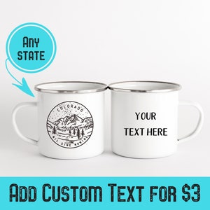 Puede incluir: Dos tazas de esmalte blanco con borde plateado. Una taza presenta una ilustraci&oacute;n en blanco y negro de monta&ntilde;as con el texto "COLORADO NIL SINE NUMINE". La otra taza tiene el texto "YOUR TEXT HERE".