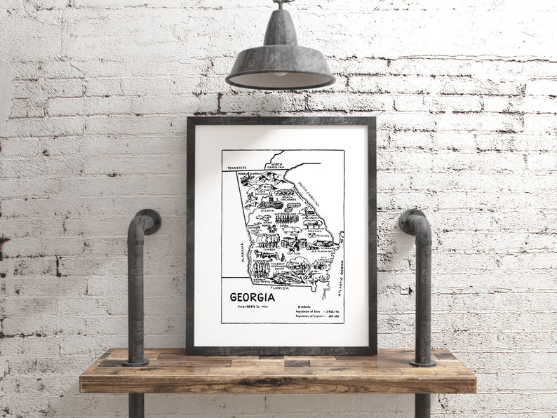 May include: Black and white illustrated map of Georgia with the state name and some details about the state. The map is framed and hanging on a white brick wall.