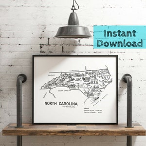 May include: A black and white illustrated map of North Carolina, showing the state's name and area in square miles. The map features various landmarks and points of interest, including the Outer Banks, the Blue Ridge Mountains, and the city of Raleigh. The map is framed in a black frame and is displayed on a wooden shelf.