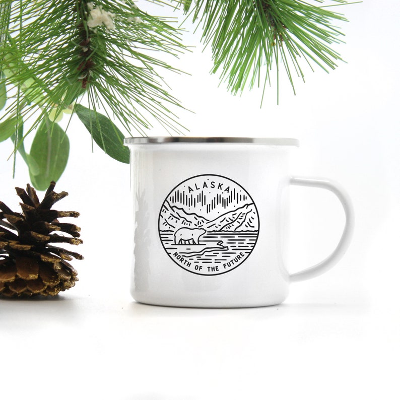 Puede incluir: Taza de camping de esmalte blanco con una ilustraci&oacute;n en blanco y negro de un oso y monta&ntilde;as. El texto "Alaska North of the Future" est&aacute; impreso en la taza.