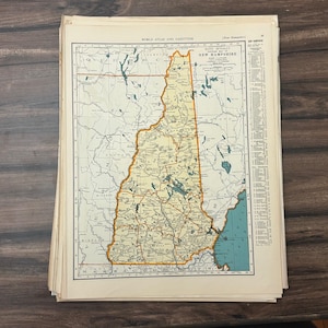 Könnte beinhalten: Ein Stapel alter Karten aus dem World Atlas and Gazetteer mit einer detaillierten Karte von New Hampshire. Die Karte ist in Beige-, Grün- und Blautönen gehalten, wobei die Umrisse des Staates orange hervorgehoben sind.