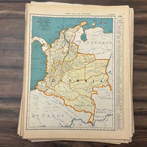 May include: A vintage map of Colombia from the World Atlas and Gazetteer. The map shows the country's borders, cities, and geographical features, with a blue and beige colour scheme. The map is part of a stack of old pages.