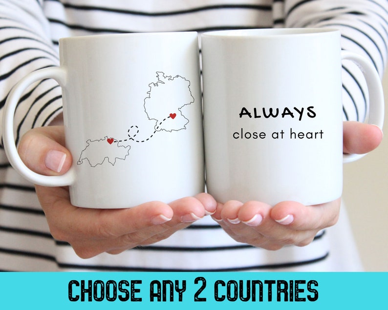 A person holding two white mugs with black graphics and text in their hands