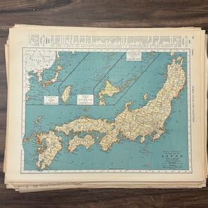 Puede incluir: Una pila de mapas antiguos de Japón, que muestran una representación detallada de la geografía del país. Los mapas están impresos en papel envejecido con una combinación de colores azul y beige. El título "Japón" es visible.