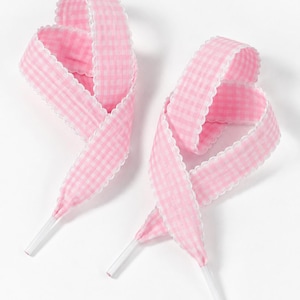 May include: Two pink and white gingham patterned shoelaces featuring a scalloped white edge trim along both sides. Each lace is looped into a decorative shape and finished with clear plastic aglets at the ends for easy threading through eyelets.