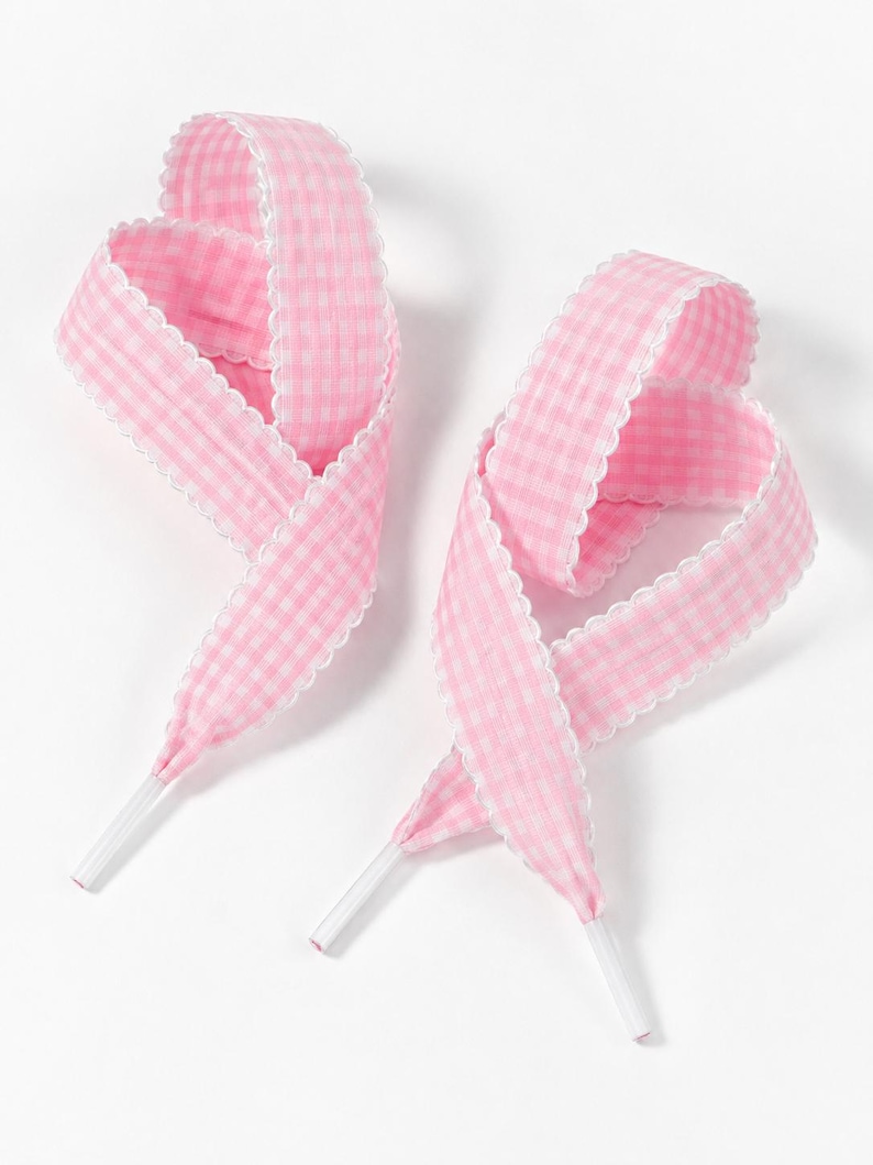 May include: Two pink and white gingham patterned shoelaces featuring a scalloped white edge trim along both sides. Each lace is looped into a decorative shape and finished with clear plastic aglets at the ends for easy threading through eyelets.