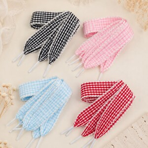 May include: Four pairs of flat shoelaces featuring a gingham check pattern in black, pink, light blue, and red. Each lace is finished with white aglets and a delicate white scalloped lace trim along both edges of the fabric ribbon material.