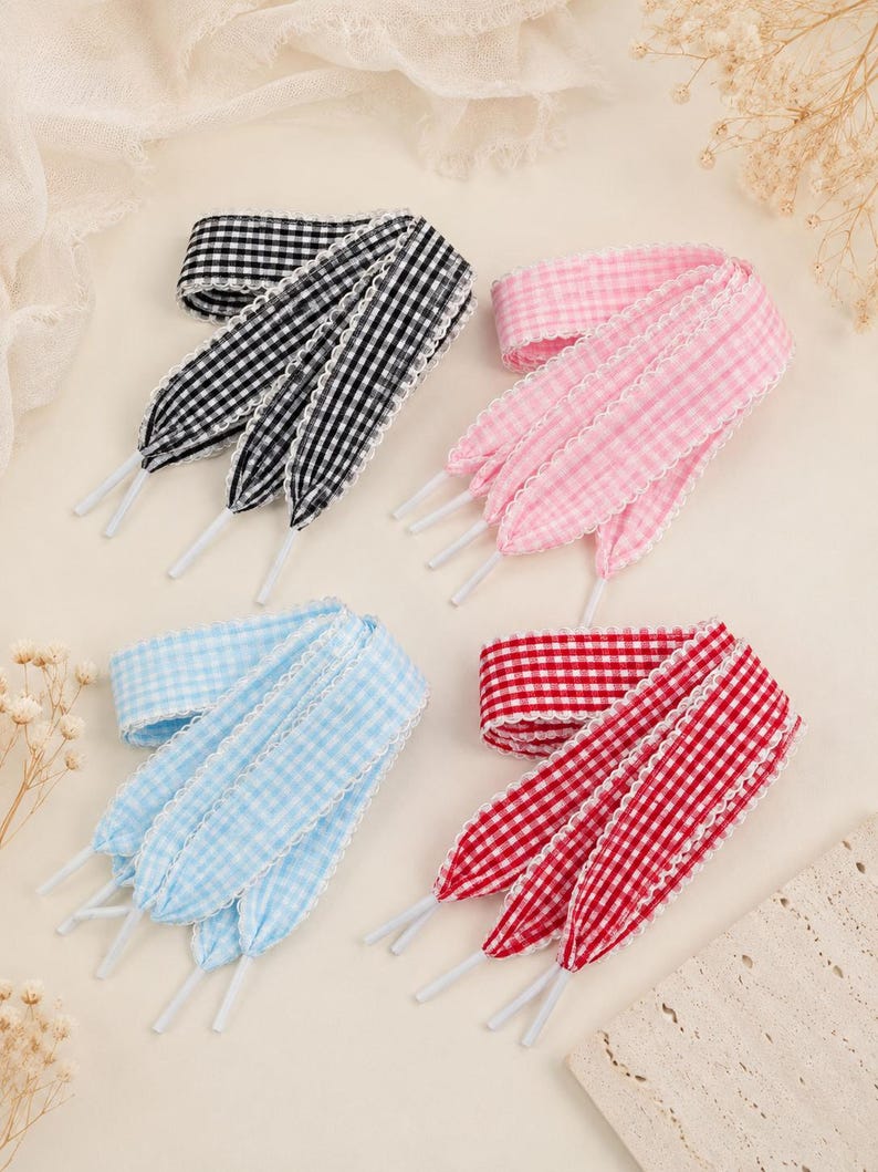 May include: Four pairs of flat shoelaces featuring a gingham check pattern in black, pink, light blue, and red. Each lace is finished with white aglets and a delicate white scalloped lace trim along both edges of the fabric ribbon material.