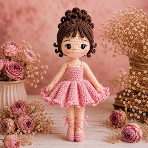 May include: A handmade crochet doll dressed as a ballerina. The doll has brown hair, rosy cheeks, and is wearing a pink tutu and ballet shoes. The background features pink roses and dried flowers, creating a soft, feminine aesthetic.