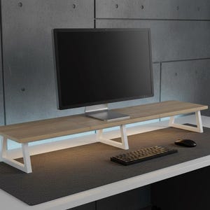 May include: A rectangular monitor stand featuring a light wood grain top surface supported by two white metal legs. The stand is positioned on a desk, holding a black computer monitor, with a black keyboard and a black computer mouse placed below.