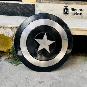 May include: A black and silver shield with a central white star design. The shield has a circular shape with a silver ring around the center and a black outer ring. The shield is a prop from the Medieval Store.