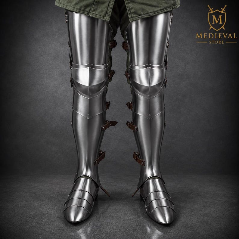 May include: Polished steel leg armor featuring articulated cuisses, poleyns, greaves, and sabatons. The armor is secured with brown leather straps and buckles along the sides. The logo for Medieval Store is visible in the upper right corner.
