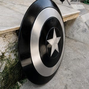 May include: A black and silver shield with a central star design. The shield has a circular shape with a silver ring around the center and a star in the middle. The shield is from Medieval Store.
