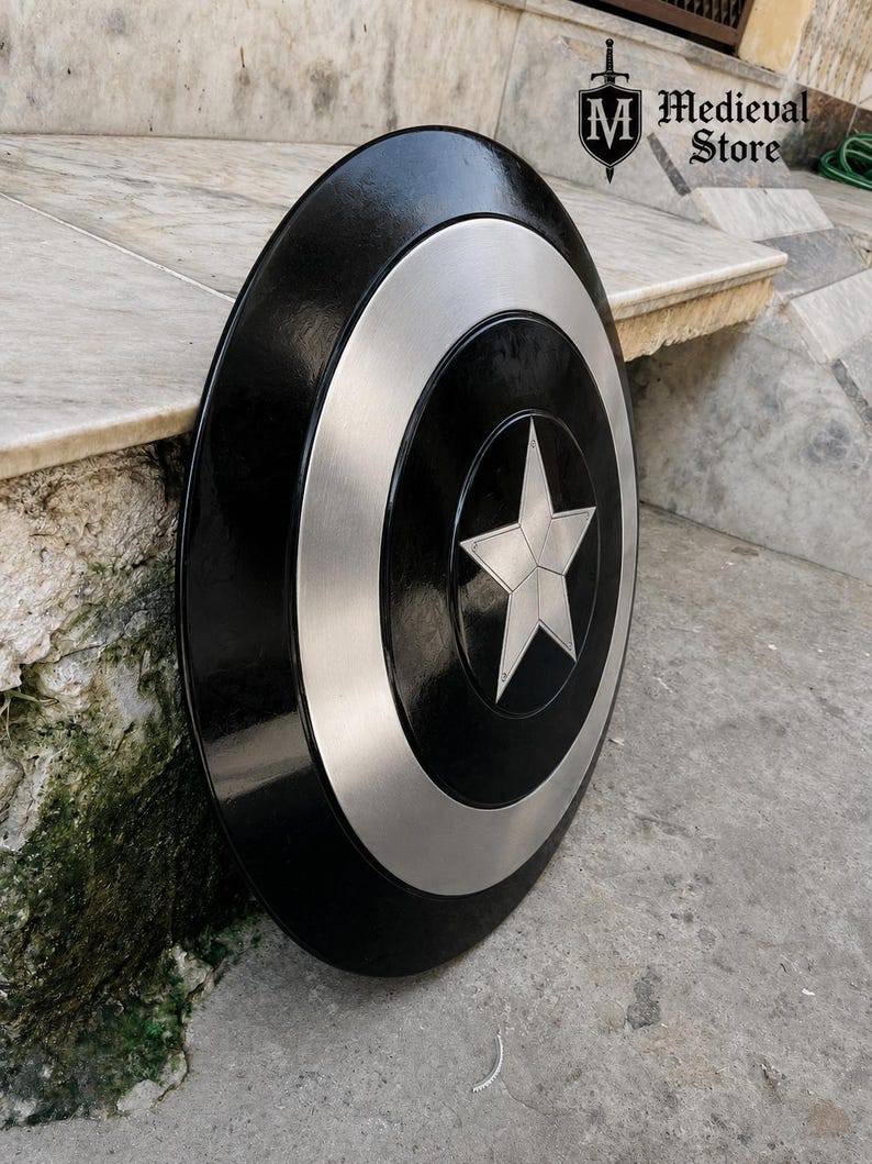 May include: A black and silver shield with a central star design. The shield has a circular shape with a silver ring around the center and a star in the middle. The shield is from Medieval Store.