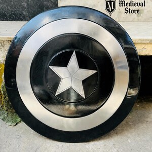 May include: A black and silver shield with a central silver star design. The shield has a circular shape with a black center, a silver ring, and a black outer edge. The Medieval Store logo is visible in the upper right corner.