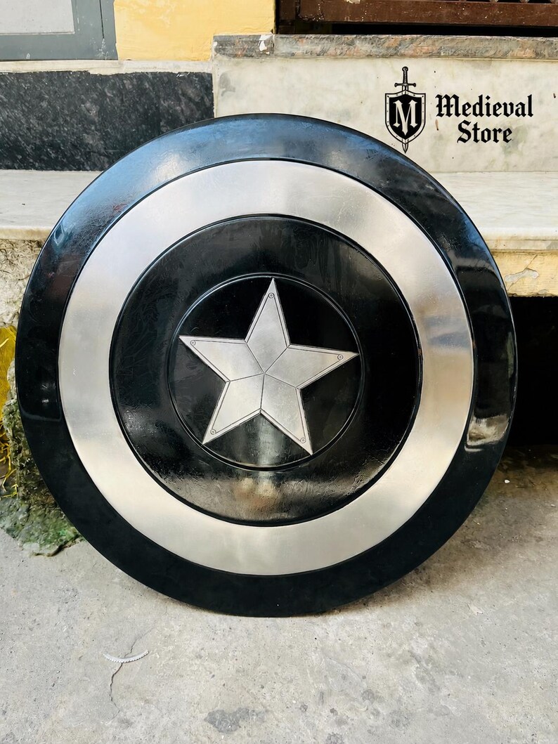 May include: A black and silver shield with a central silver star design. The shield has a circular shape with a black center, a silver ring, and a black outer edge. The Medieval Store logo is visible in the upper right corner.
