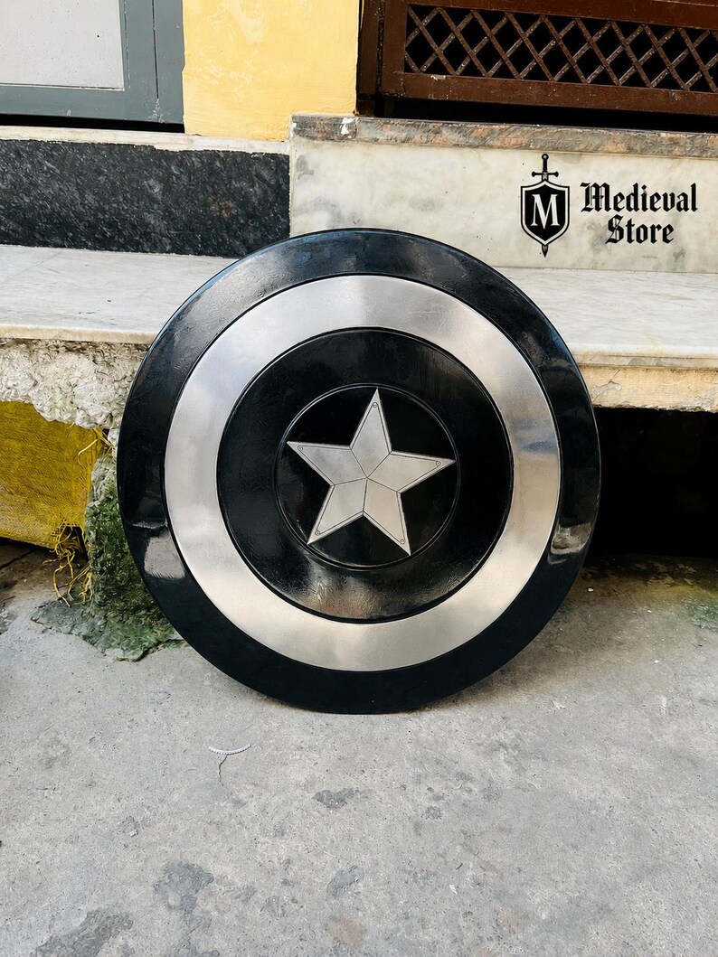 May include: A black and silver shield with a central white star design. The shield has a circular shape with a silver ring around the center and a black outer edge. The shield is a prop from the Medieval Store.
