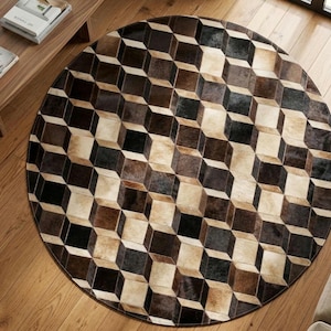 May include: A circular area rug featuring a geometric pattern of cubes in shades of dark brown, light brown, cream, and black. The rug is constructed from individual panels of hair-on hide, creating a textured surface with a repeating 3D cube effect.