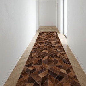 May include: A long rectangular runner rug featuring a geometric pattern composed of stitched leather patches in various shades of brown, ranging from light tan to deep chocolate, creating a three-dimensional cube effect across the surface.