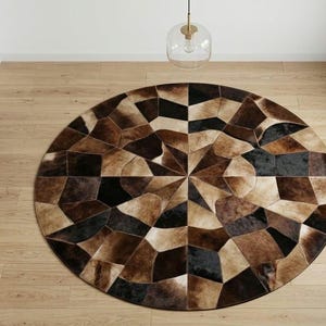 Könnte beinhalten: Ein runder Teppich, der aus einem Patchwork von Kuhfellstücken in verschiedenen Braun-, Schwarz- und Cremetönen besteht. Die einzelnen Fellsegmente sind in einem geometrischen, radialen Muster angeordnet, das von der Mitte ausgeht.