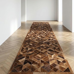 Könnte beinhalten: Ein langer, rechteckiger Läufer mit einem geometrischen Muster aus verschiedenen braunen, beigen und dunkel schokoladenfarbenen Kuhfellstücken. Das Design besteht aus aneinandergenähten Dreiecken, Rauten und kreisförmigen Segmenten.