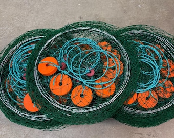 May include: Three green fishing nets with orange floats and turquoise rope. The nets are circular and appear to be made of a durable material. The floats are evenly spaced within the nets, and the rope is coiled.